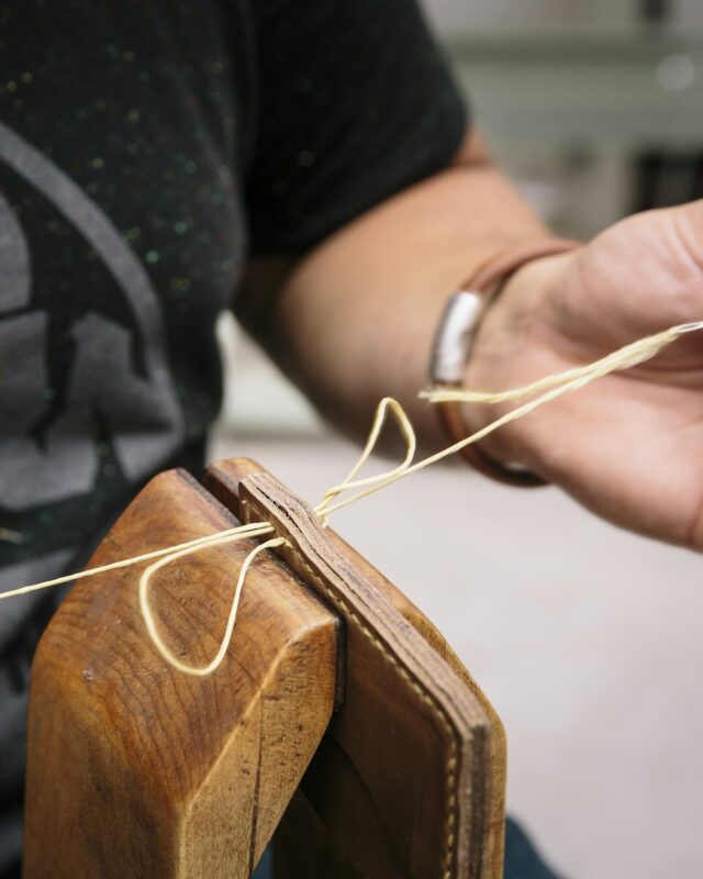 Hands saddle-stitching a leather panel by hand